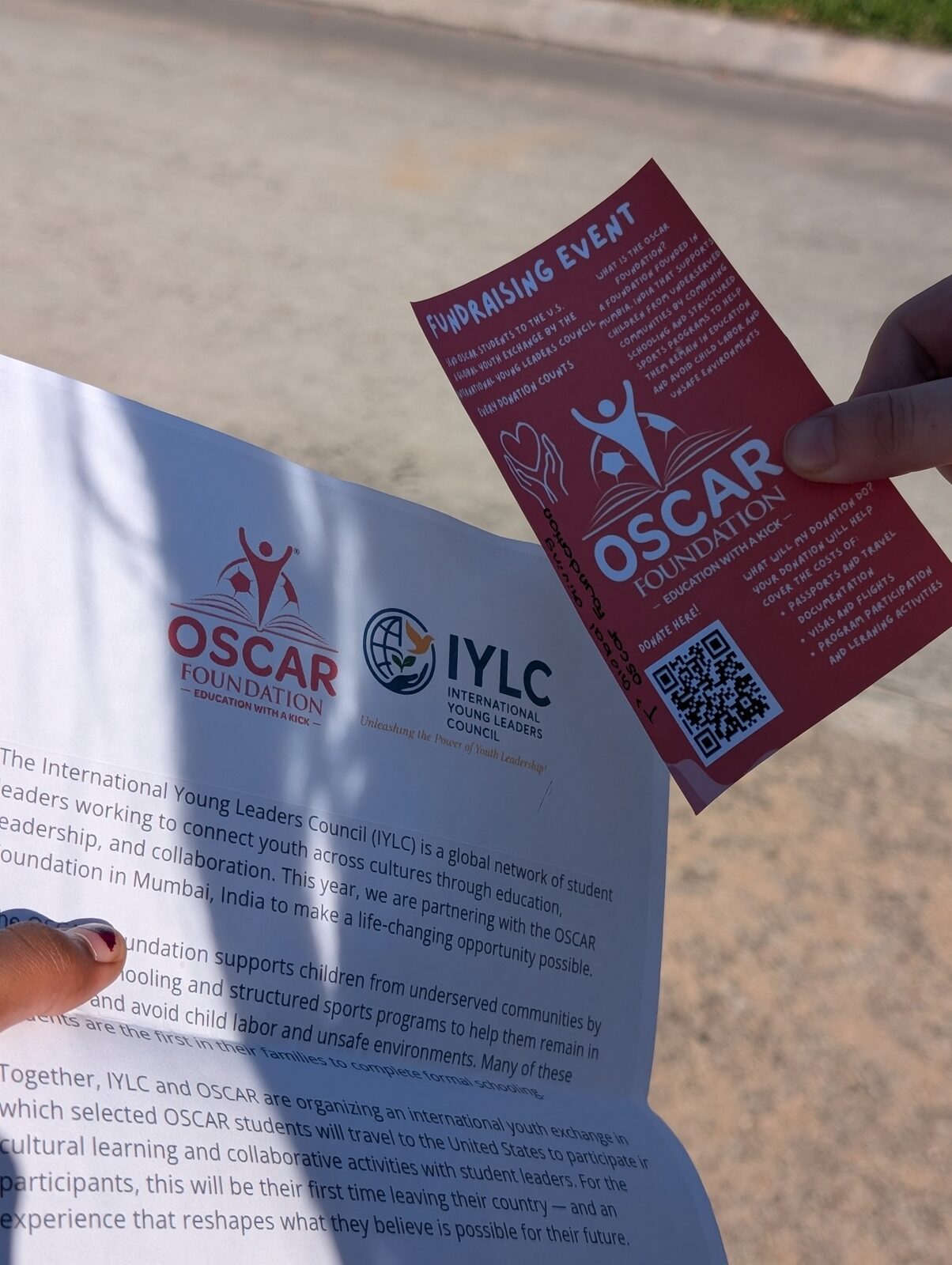Hands holding printed IYLC and OSCAR Foundation campaign flyers outdoors