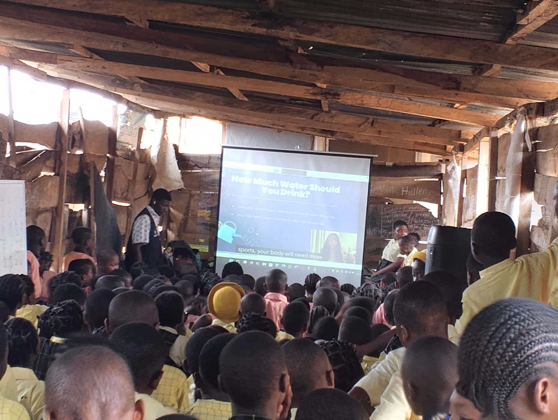Young children seated closely together watching a Teen2Teen video about how much water to drink