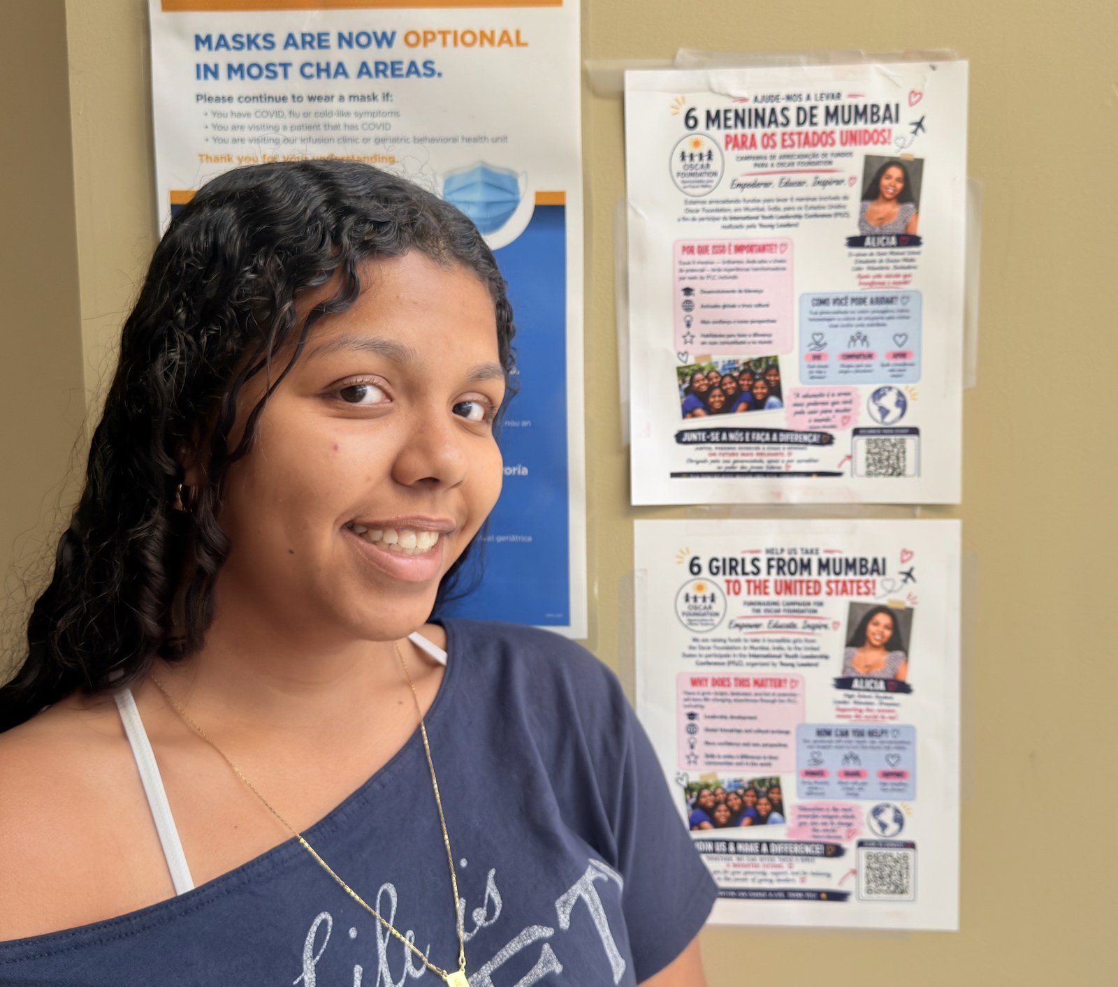 An IYLC student standing beside her OSCAR campaign flyers posted in English and Spanish on a community board