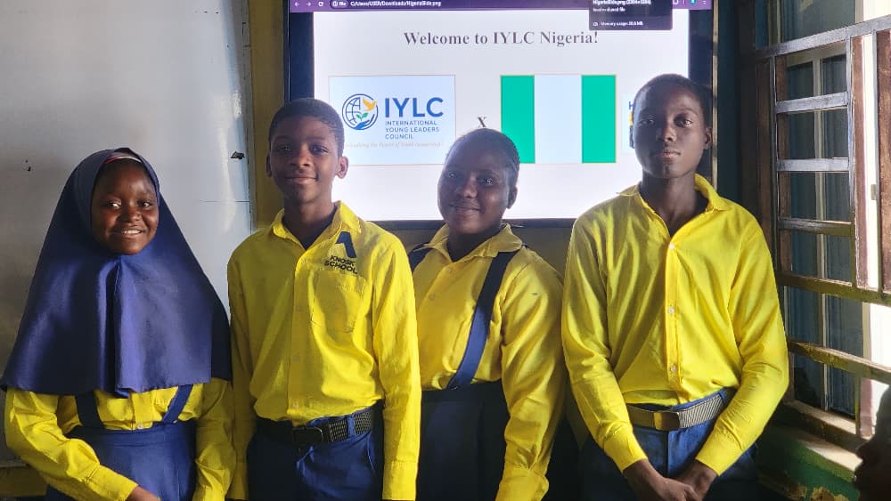 Students in school uniform in front of a screen reading Welcome to IYLC Nigeria